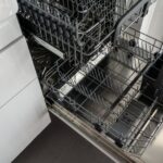 A clean and empty stainless steel dishwasher open in a modern kitchen setting.